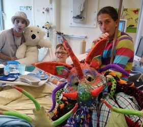 2Faced Dance's colourful dragon and two other performers interact with boy in bed