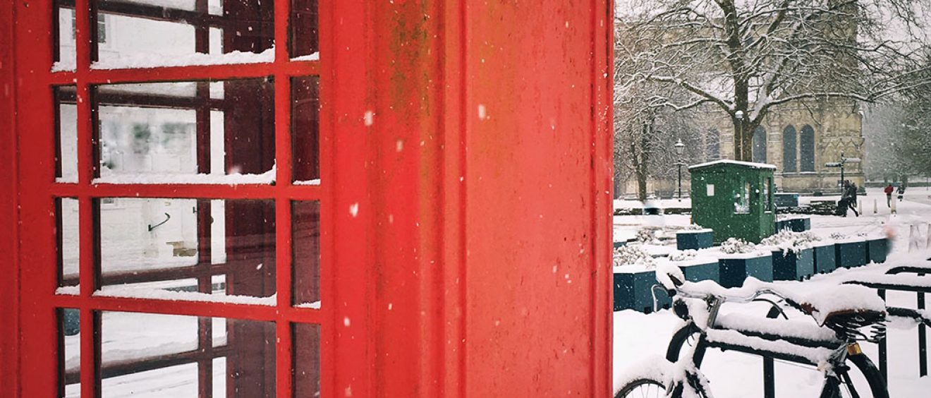Photo of red telephone box next to a bike with cathedral in the background in the snow