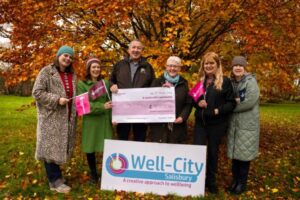 Team from Well-City pose with a large cheque in front of autumn trees