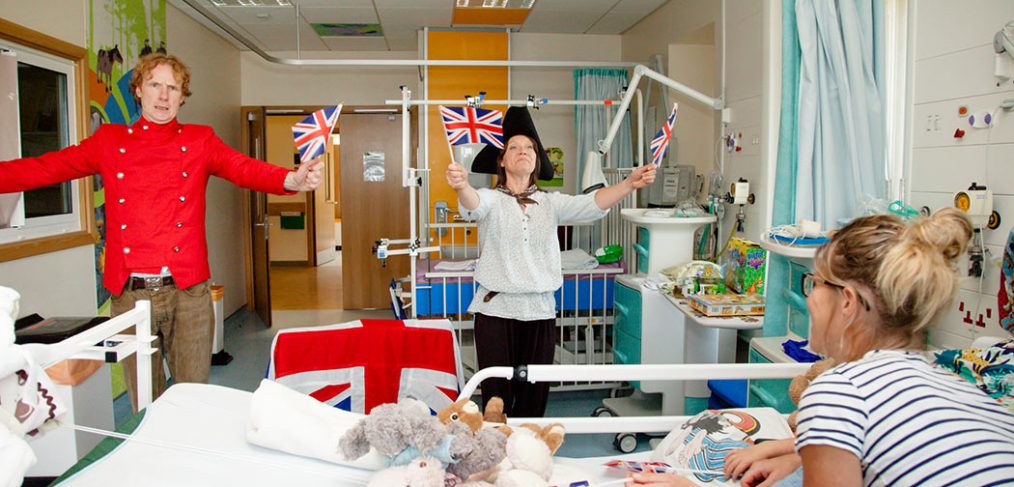 Actors dressed as pirates waving flags, parent and child on ward watching