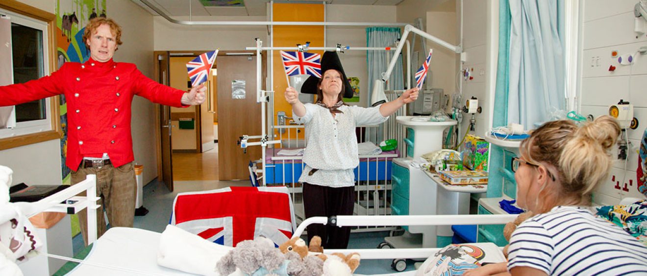 Actors dressed as pirates waving flags, parent and child on ward watching