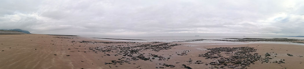 panoramic of beach looking out to sea, large expanse of sand, cloudy skies