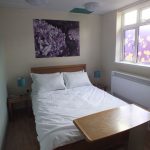 wooden double bed, bedside table lamps, artwork and coloured ceiling tiles, bespoke flower design window film