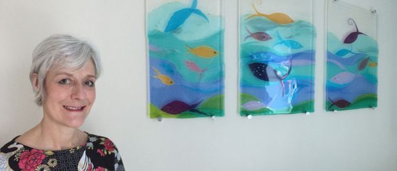 Sue King with her tryptich of fused glass panels showing fish amongst waves