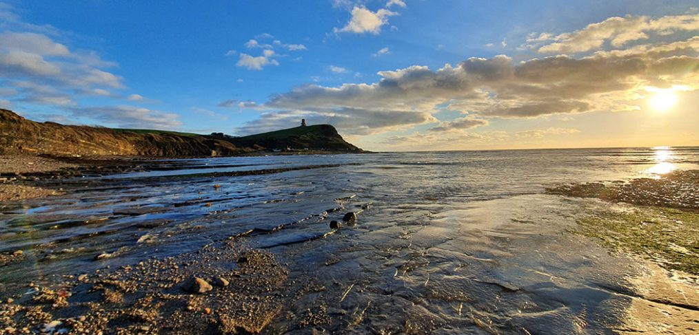 sun rising over Kimmeridge bay, low tide foreground, cliff in distance
