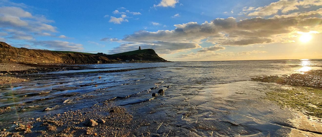 sun rising over Kimmeridge bay, low tide foreground, cliff in distance