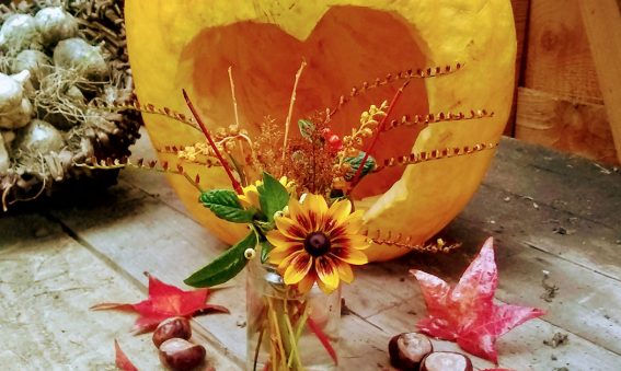 pumpkin with heart shape carved out, conkers, leaves and a posy of flowers and stems in a jam jar