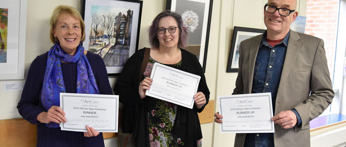 Mary Fawcett, Joanne Tudor and Fred Fieber holding certificates in front of the exhibition