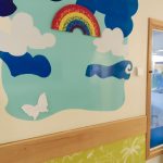 Butterfly rainbow print on wall with cut out shaoes of sky and clouds and a butterfly ready for messages from parents and staff