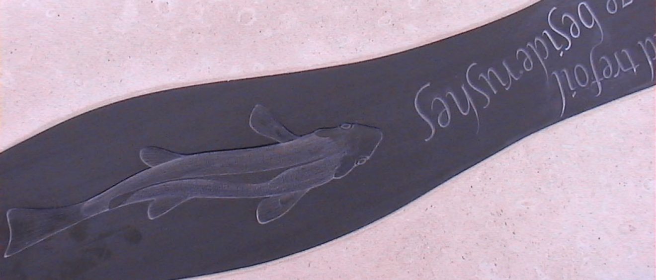 close up detail of slate bench showing carved fish and words from poem
