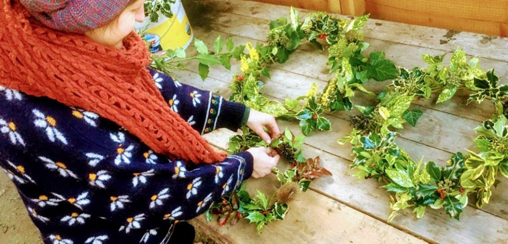 Hannah in winter woollies putting finishing touches to wreaths made from leaves and berries
