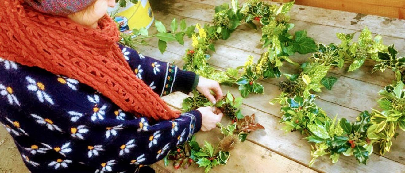 Hannah in winter woollies putting finishing touches to wreaths made from leaves and berries